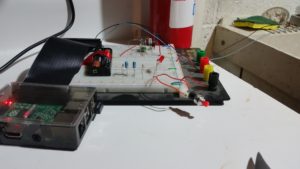 Raspberry Pi connected via ribbon cable to breadboard.  Breadboard has several circuits on it, and is sitting on a table.  Two wires run from breadboard to slop sink to the right.