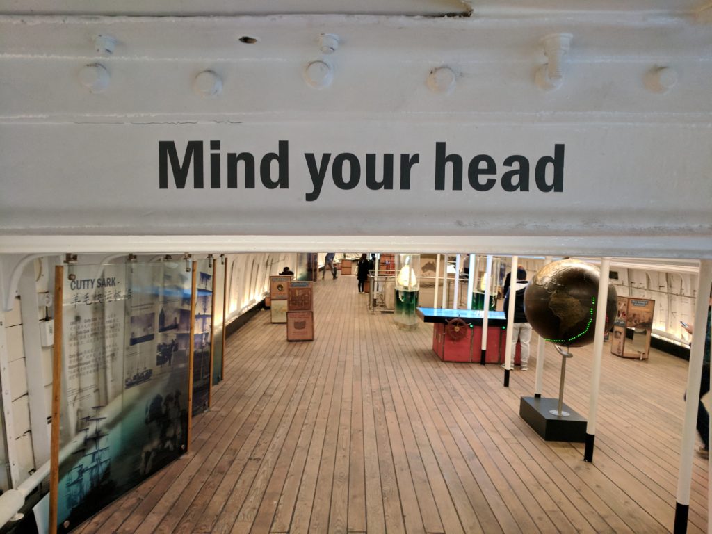 A warning sign is painted on the metal beams of the Cutty Sark, warning folks to watch their head. The story of my life.